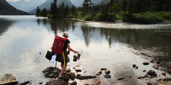 Hiker crossing outlet Cosley Lake, Glacier Nationa